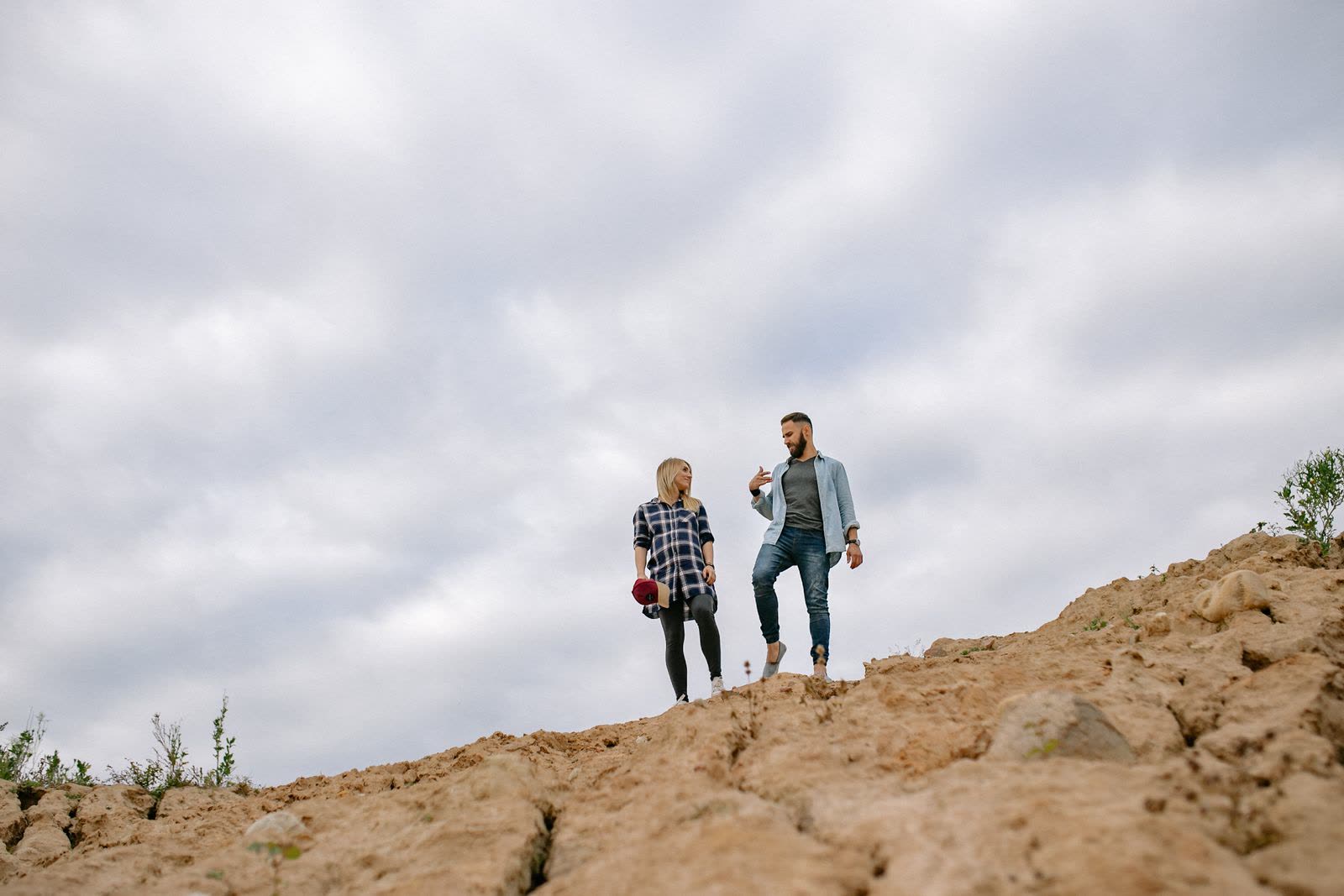 Couple walking along a ridge of sand seen from below against a cloudy sky
