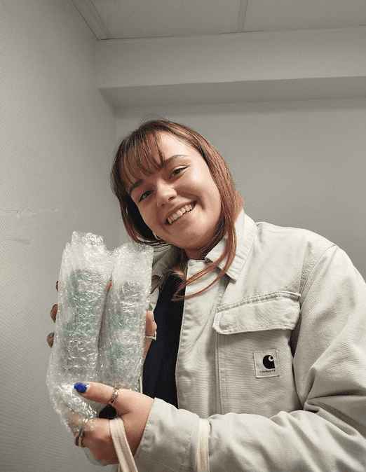 A smiling woman with her arms crossed, standing against a dark green background. She has long, dark hair.
