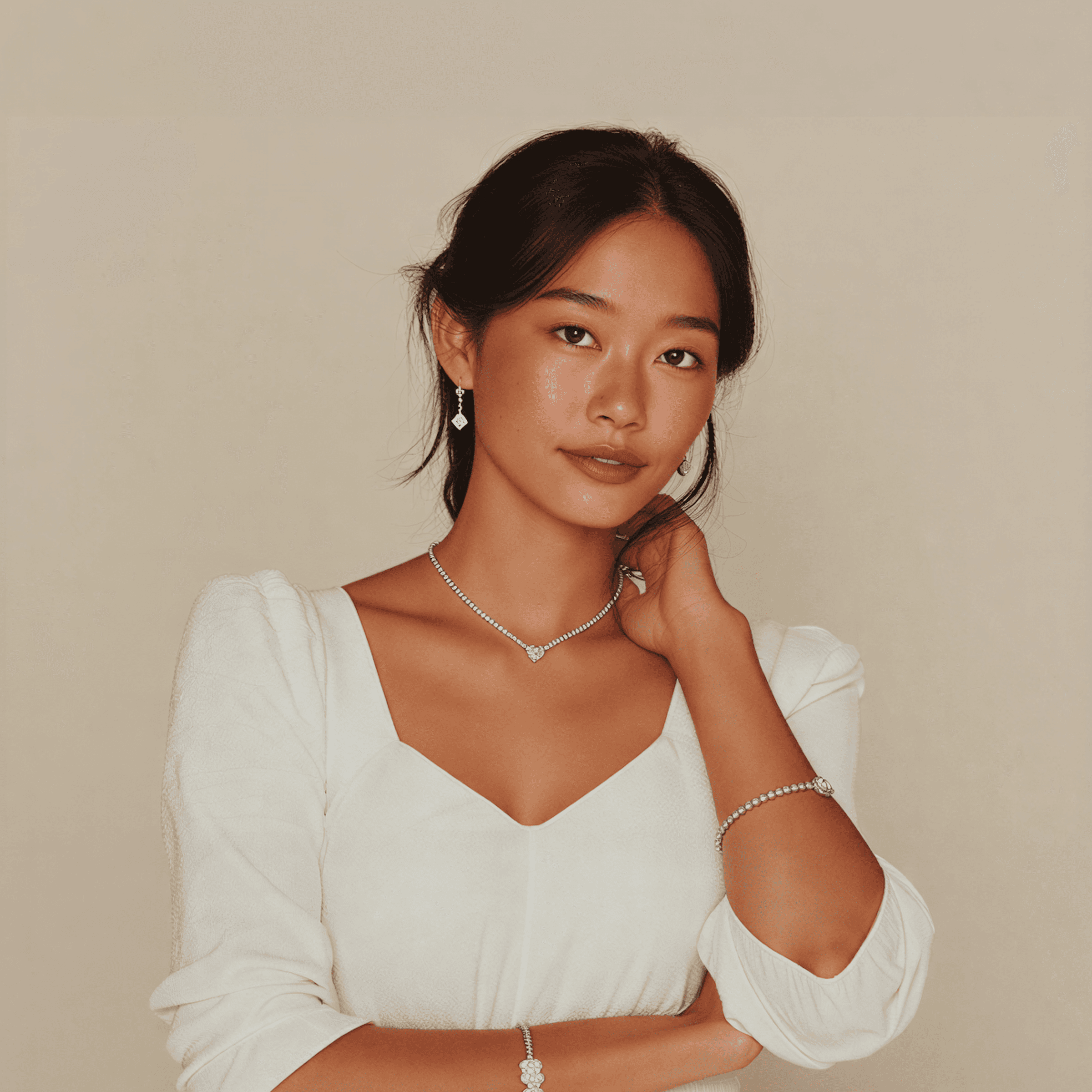 A young person poses thoughtfully with one hand on their chin, wearing a white top against a neutral background.