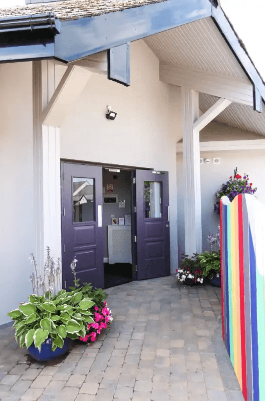 Entrance to a colorful building with purple doors, flowers, and a rainbow-colored fence.