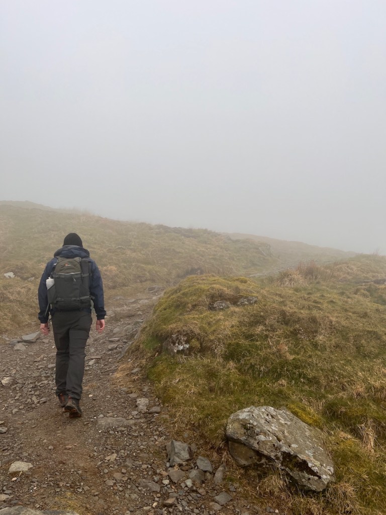 The back of Martin walking up a stony path leading into fog.