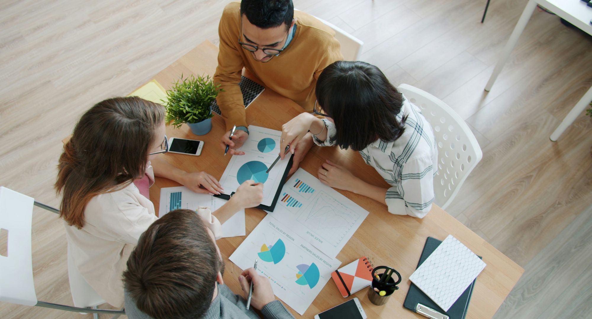 equipe colaborando em torno de uma mesa com tabelas e gráficos sobre