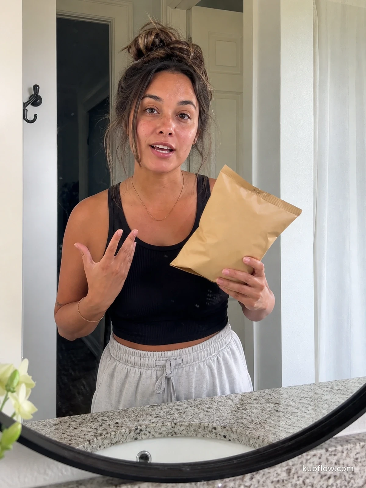UGC-style photo: small business owner creator, in a bathroom mirror setup, holding a generic snack bag while talking to camera, slightly wider waist-up shot.