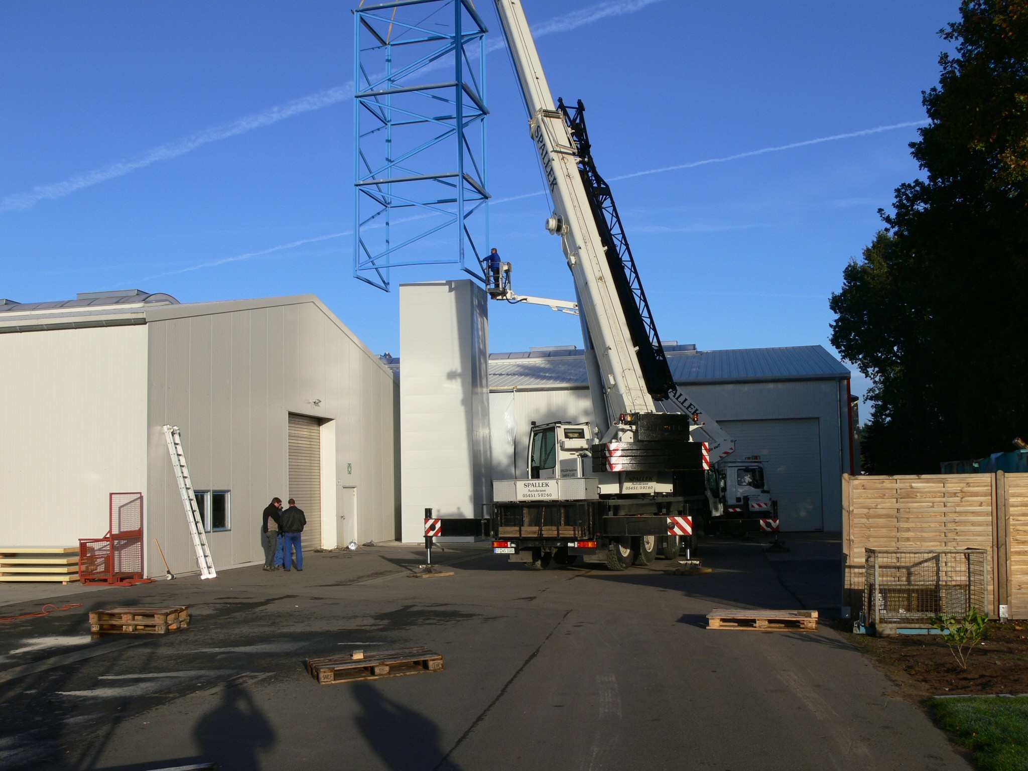 Kran hebt Metallkonstruktion auf Gebäude. Bauarbeiten, Industriehalle im Hintergrund.