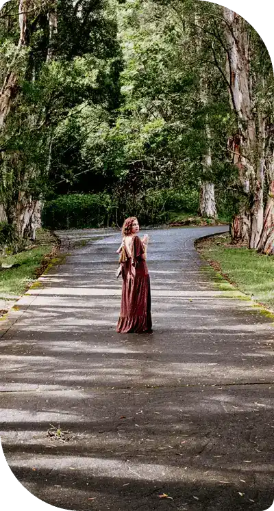 Woman walking down a mystical tree-lined path surrounded by ancient oaks draped in Spanish moss, symbolizing the transformational journey and hero's quest