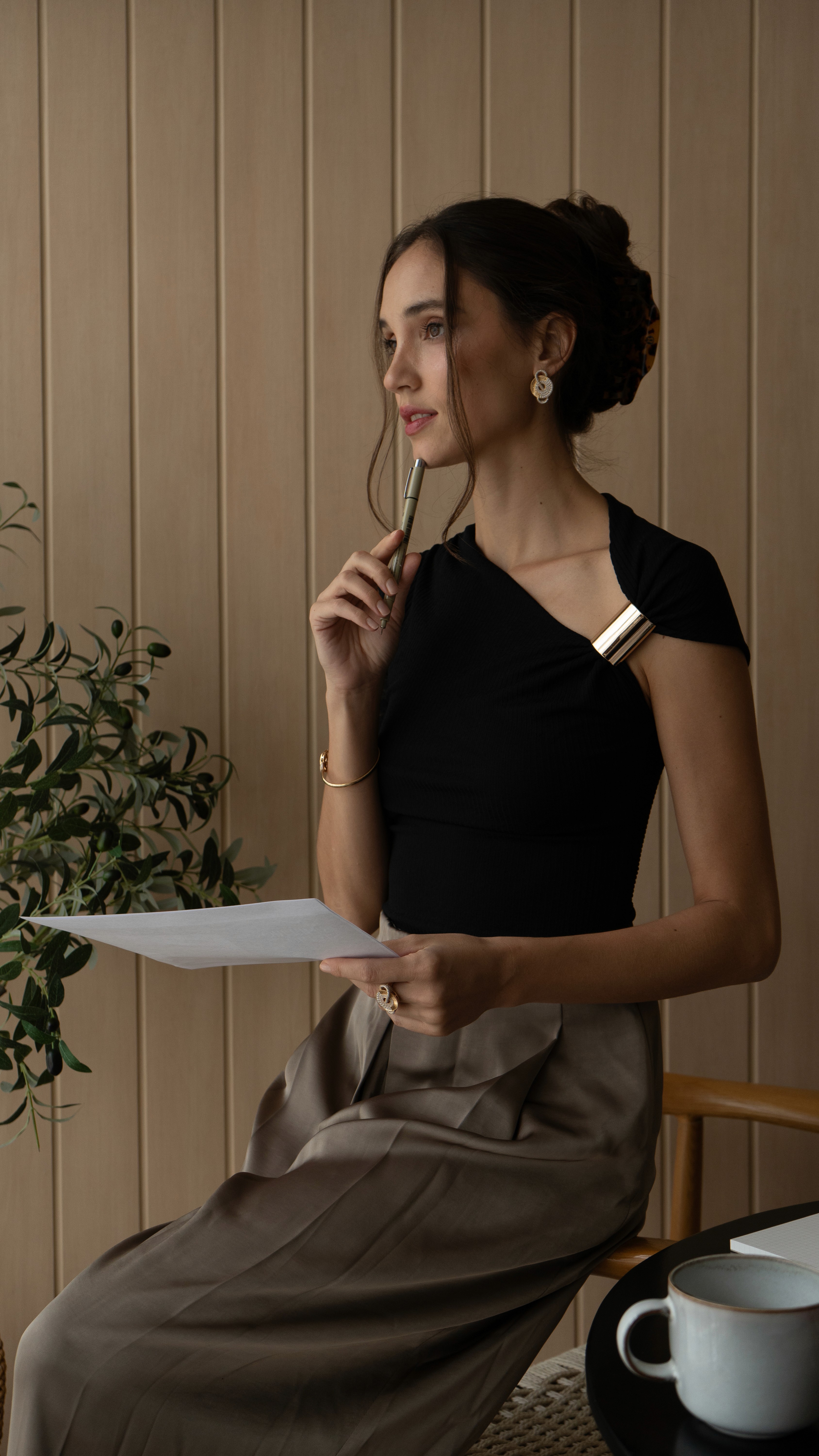 A gold charm necklace with small coin pendants laid across a brown book and white fabric.