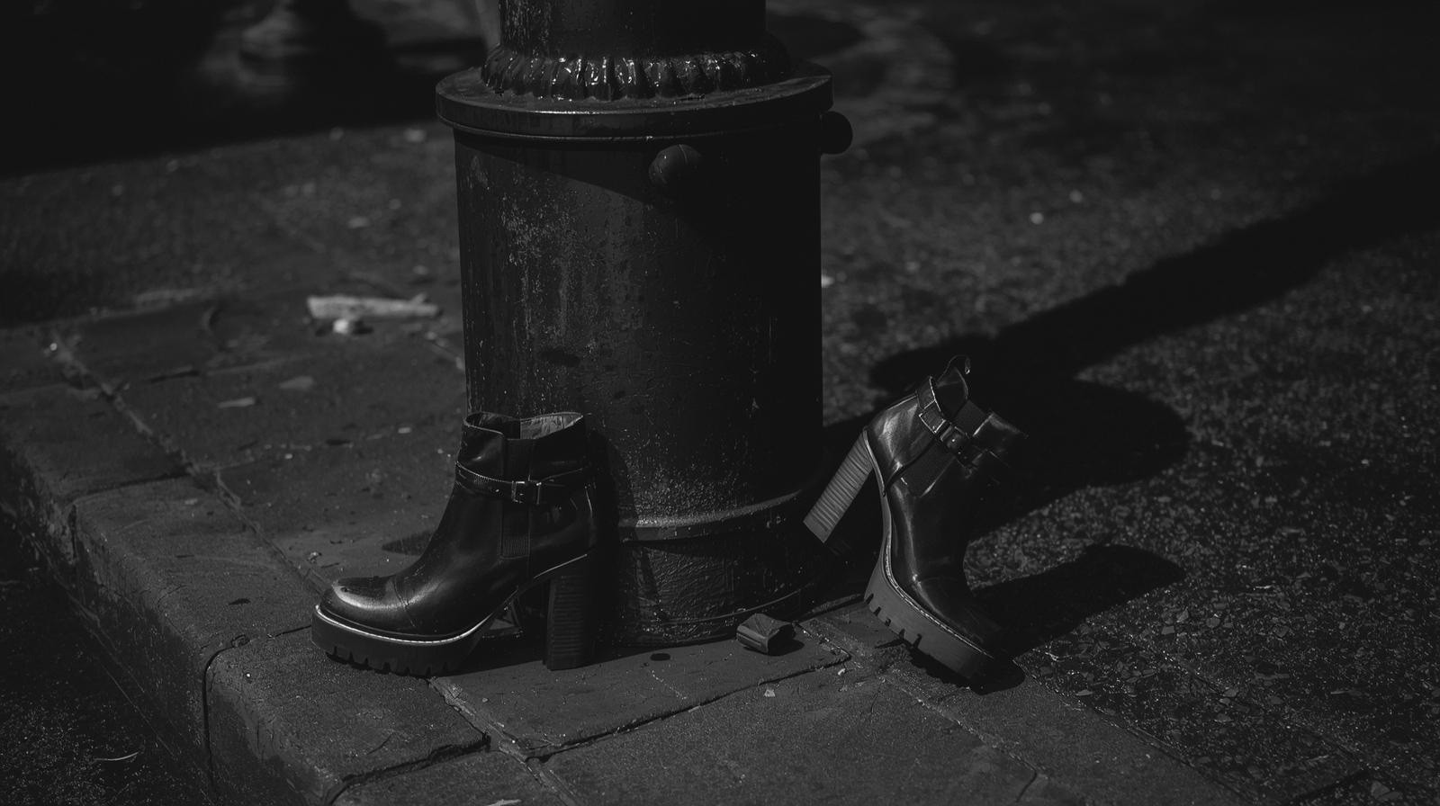 Scarpe usurate lasciate sul marciapiede in un contesto urbano, illuminazione notturna.