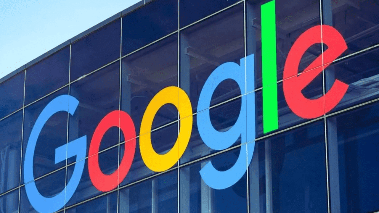 Google logo displayed on the glass facade of a building, featuring bold, colorful letters in blue, red, yellow, and green against a reflective background.