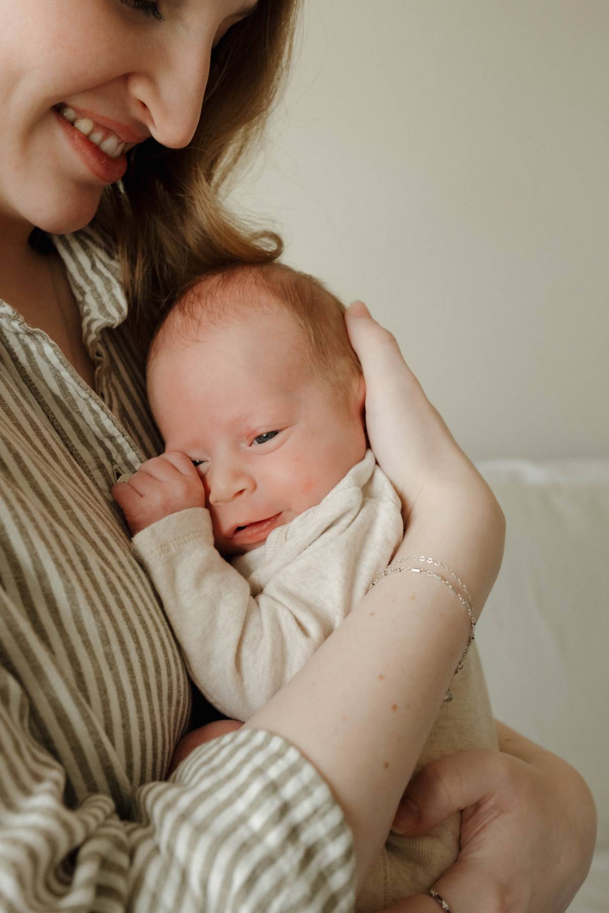 Close-up of a smiling mother holding her newborn baby, looking tenderly at the infant in a cozy, natural light setting during a newborn photoshoot in Gilbert, Arizona.