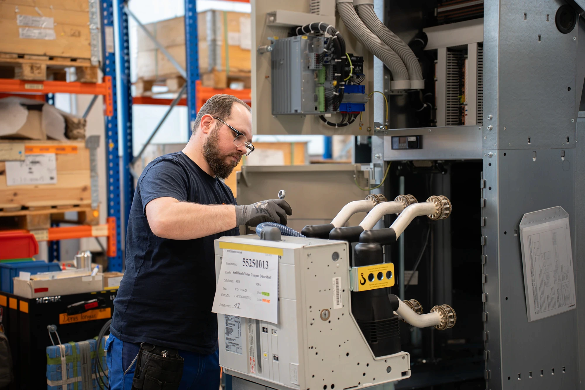 Ein Mitarbeiter von RITTER Starkstromtechnik wartet eine elektrische Schaltanlage in der Produktionshalle. Er prüft und montiert Komponenten an einer geöffneten Mittelspannungsschaltanlage.