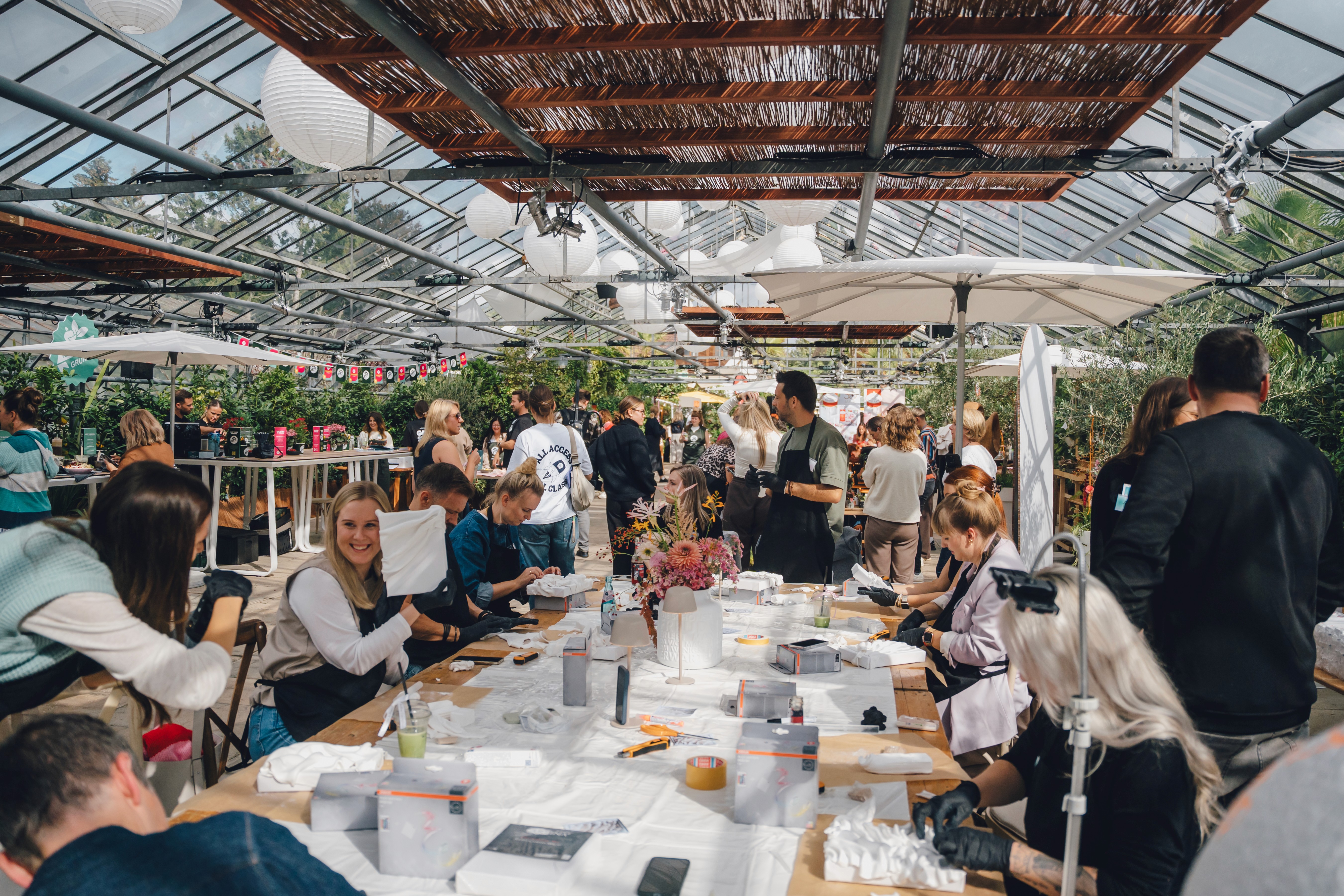 Großer Kreativ-Workshop mit Teilnehmerinnen an langen Tischen in einem lichtdurchfluteten Glashaus.