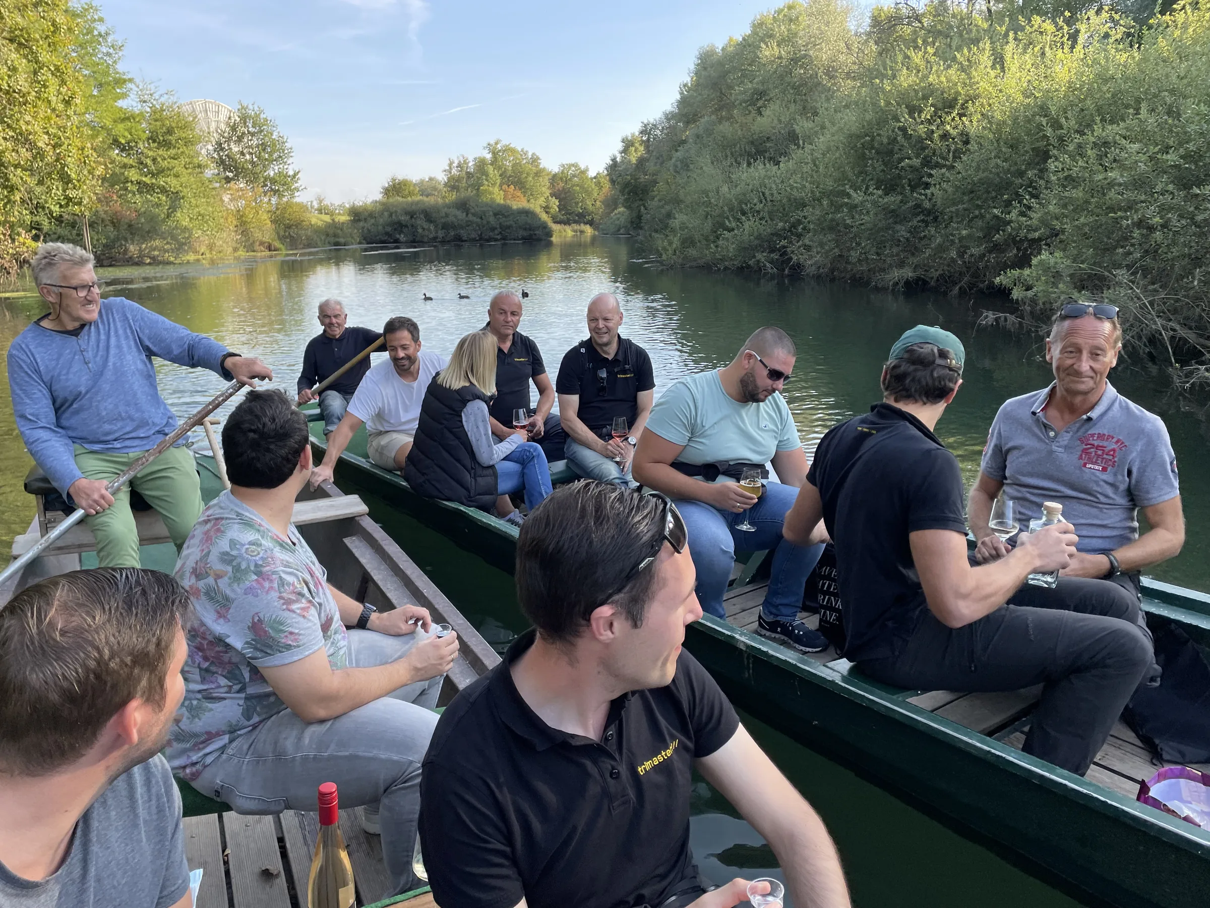 Team sitzt in einem Weidling auf einem Fluss und wird über ruhiges Wasser gestakt