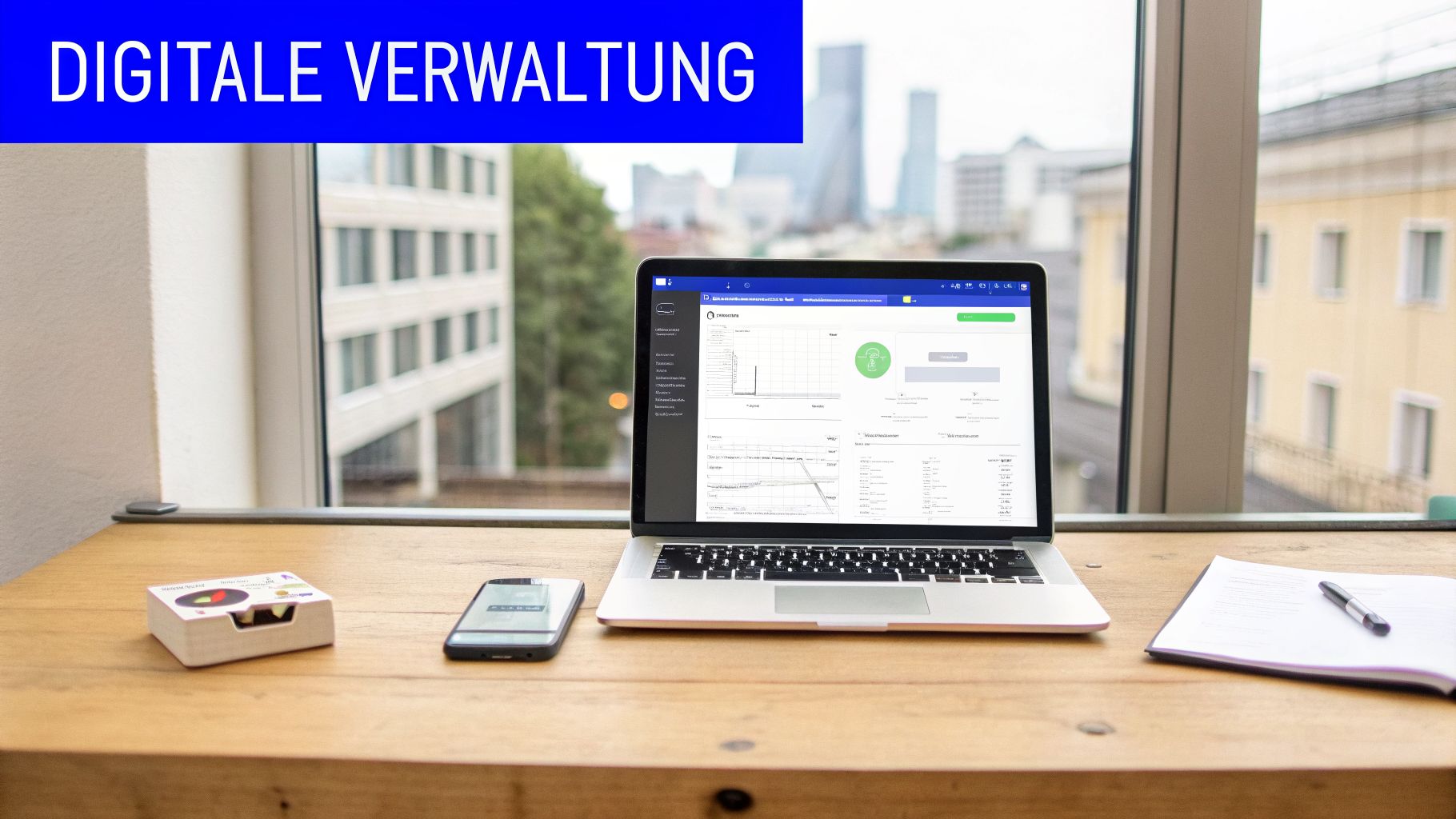 Laptop auf Holzschreibtisch mit Blick auf Stadtlandschaft, darauf läuft digitale Verwaltungssoftware, daneben Smartphone und Notizblock.