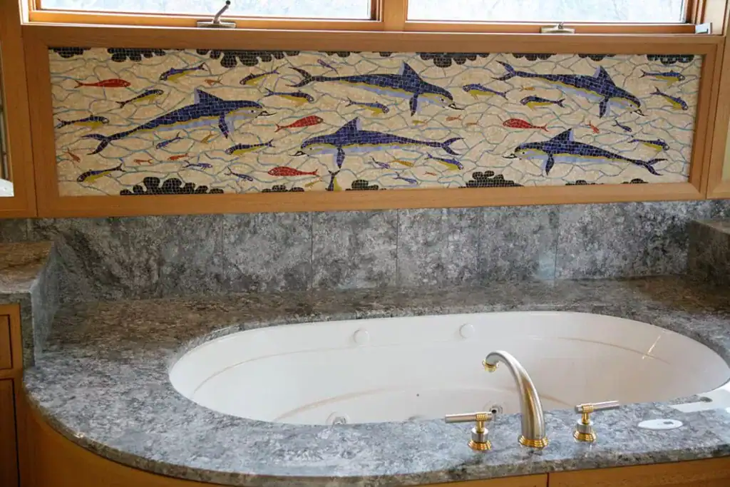 Colorful mosaic fish art panel above bathtub in Mosaiclegs Art Studio.