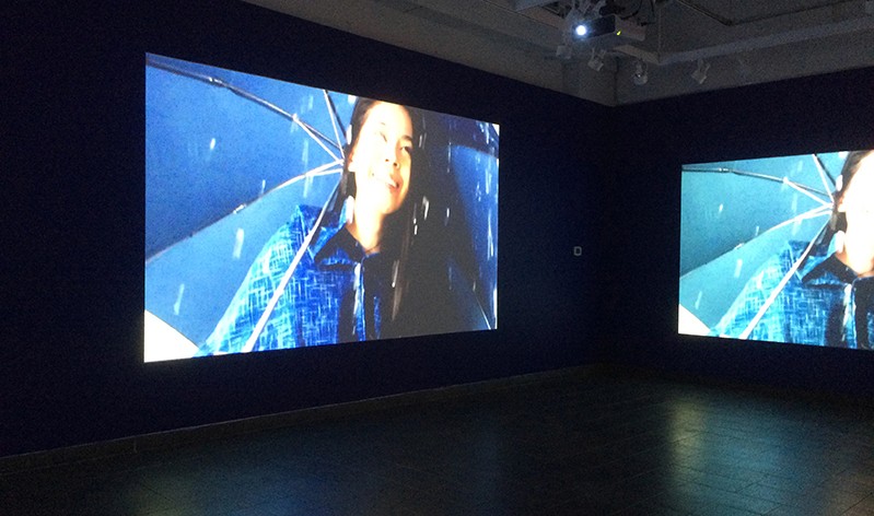 an image of a woman with a blue umbrella projected on two walls in a dark room
