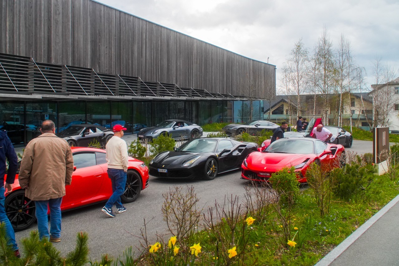 Voitures de sport rouges et noires garées devant un bâtiment moderne en bois, participants autour