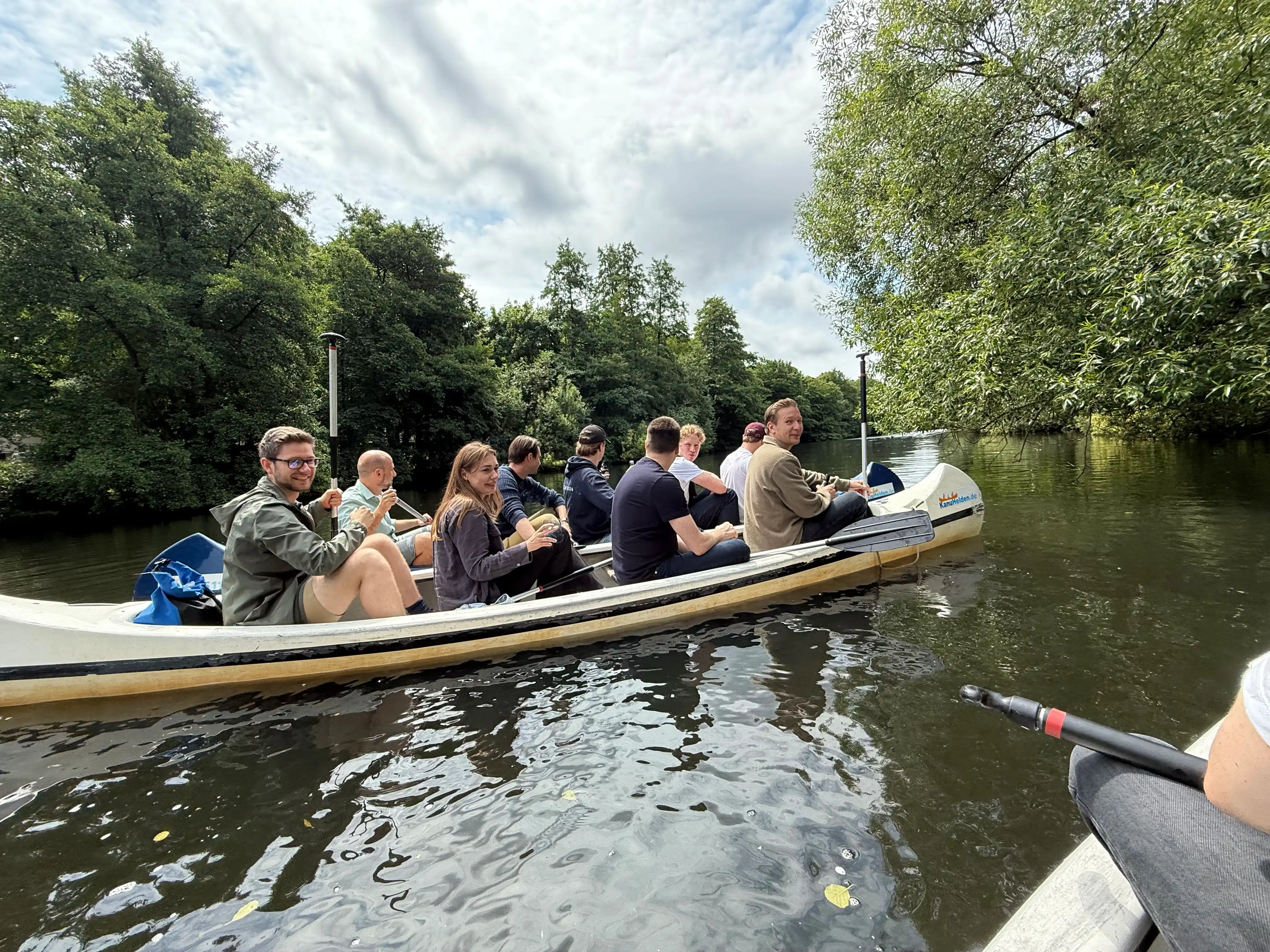 Group of people paddling together in a canoe on a calm river surrounded by trees