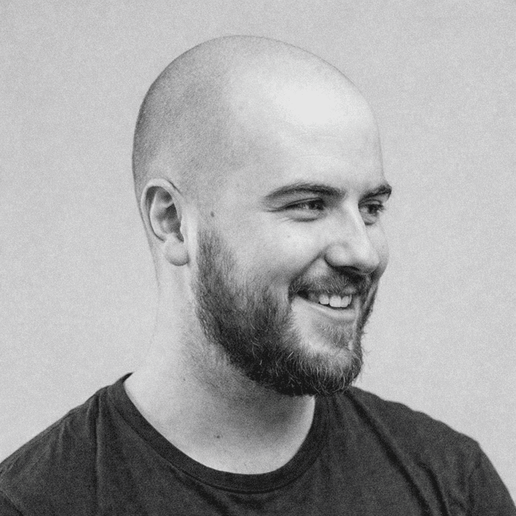 Portrait of a young man with short hair, wearing a dark t-shirt, against a plain background.