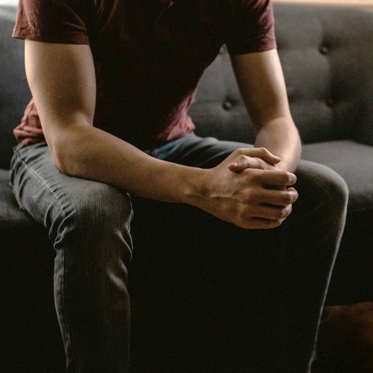 A man sitting on a couch with his hands clasped resting on his knees