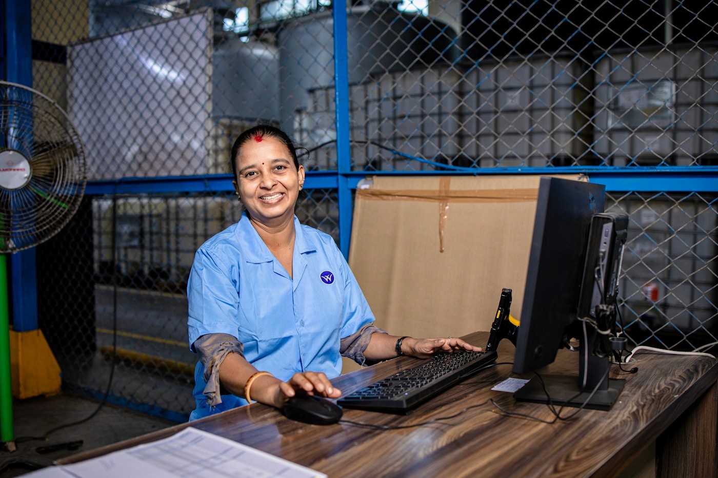 Indian factory worker smiling at a computer terminal on the shop floor, representing ERP software in use