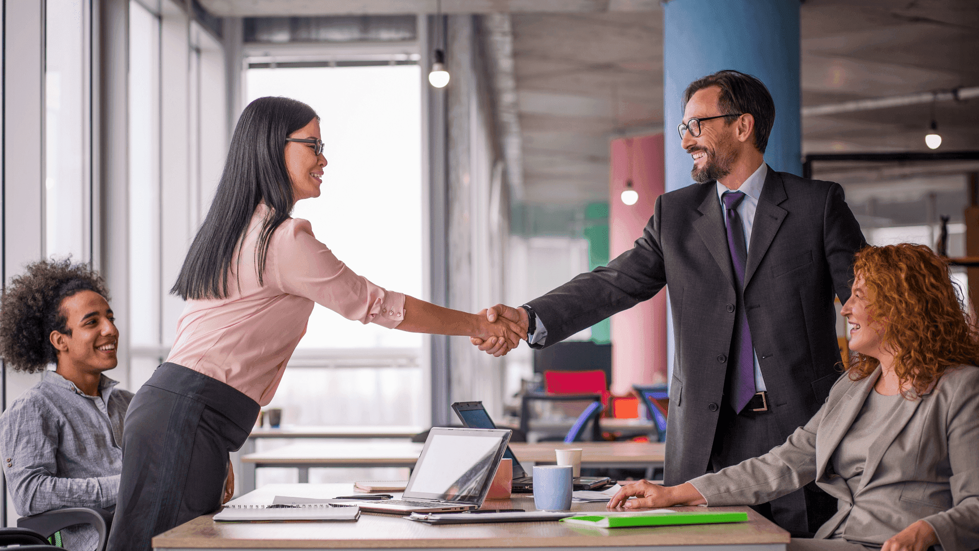 Business professionals shaking hands in a modern office during a successful client onboarding meeting, representing real-time customer screening and UK FCA compliance expectations.