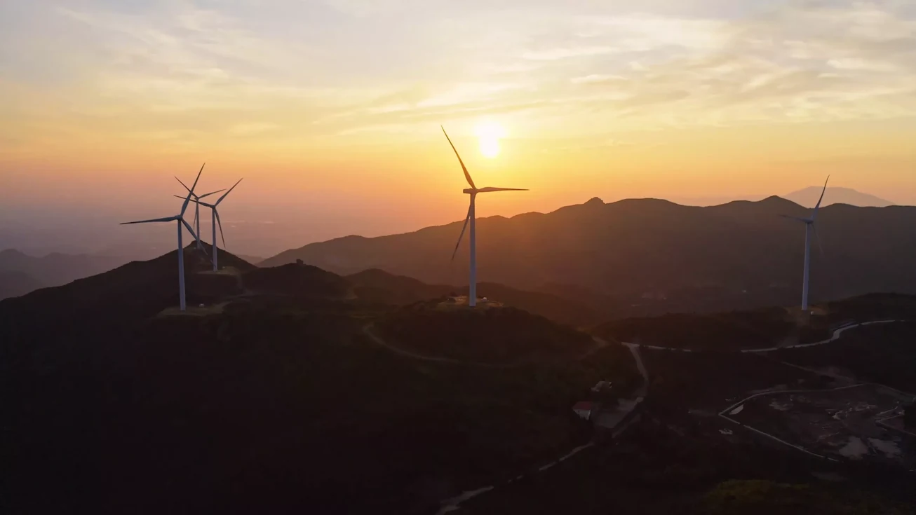 A wind turbine on a mountain ridge at sunset