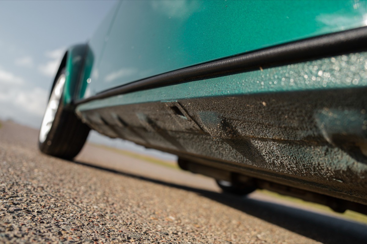 Close-up of a car's tire and undercarriage on a dirt road, with a clear sky in the background.