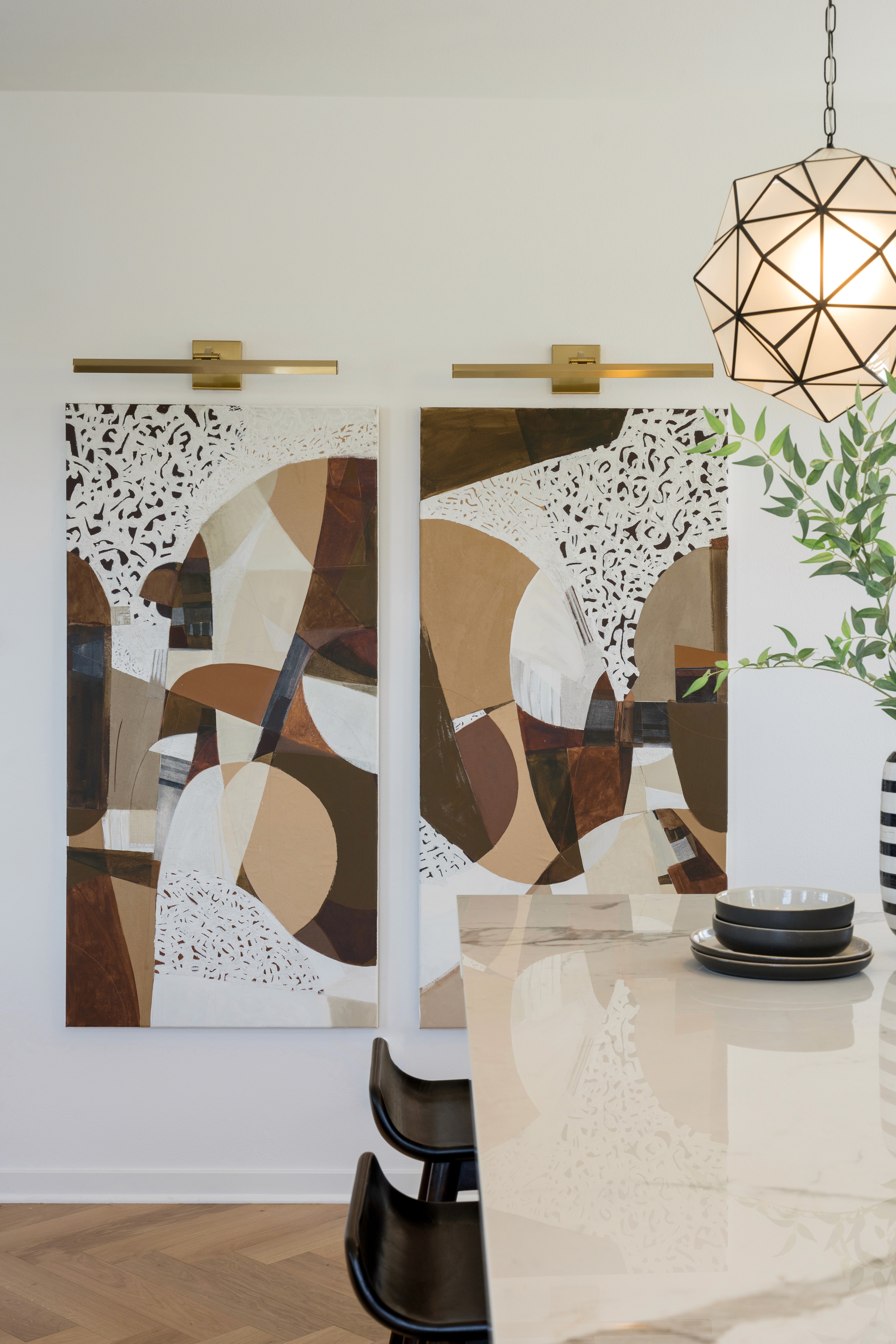 White marbled kitchen island with black stained wood counter stools and modern artwork with sconce lighting