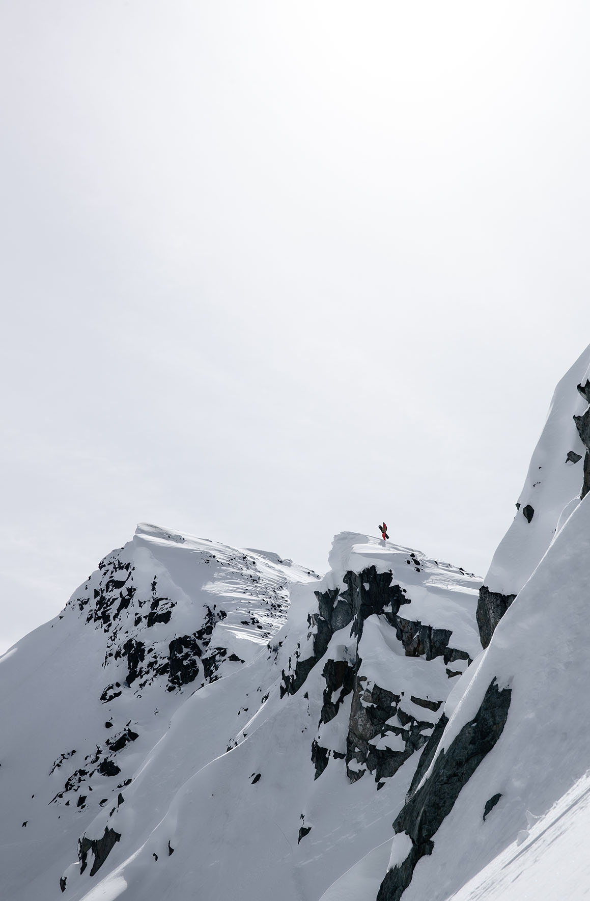 Snowboarder holding their board on the edge of a cliff in the mountains of Whistler, Canada.