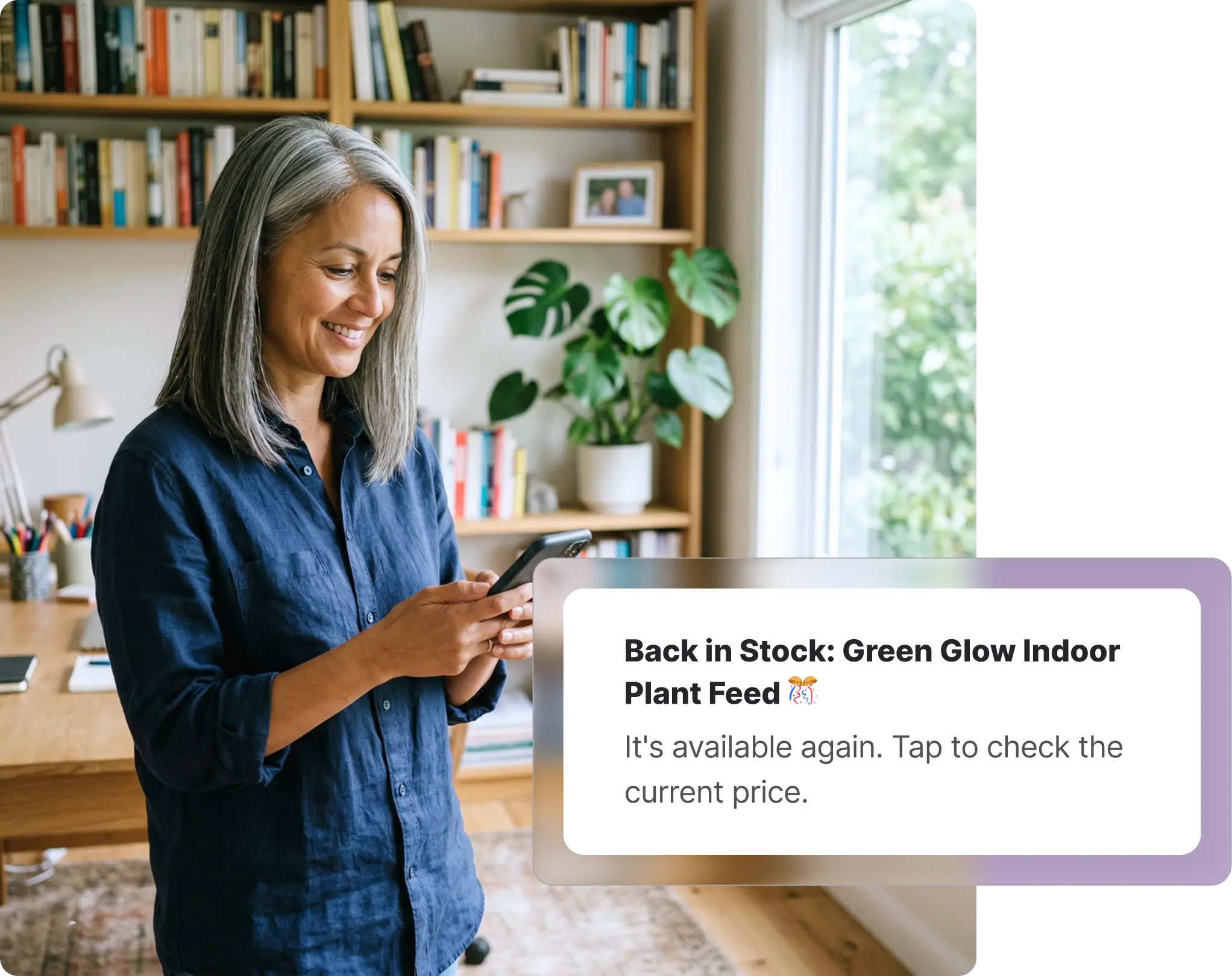 A smiling, middle-aged woman with grey hair standing in a cozy home office, looking at her smartphone. Behind her, a large wooden bookshelf filled with books and a desk with a lamp are visible near a window. Overlaid on the image is a Whisprice digital notification displaying a back-in-stock alert for an Amazon product, specifically the "Green Glow Indoor Plant Feed," prompting the user to tap and check the current price.