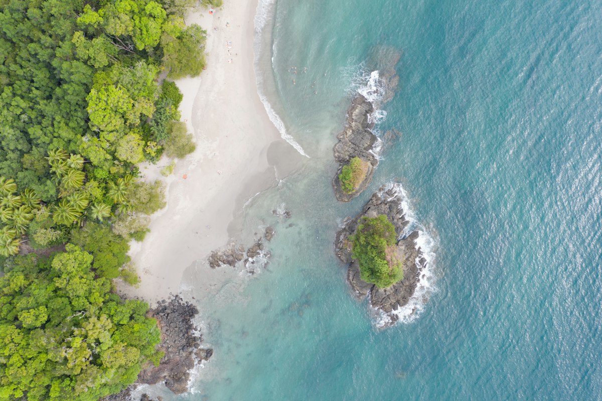 Aerial view of a white-sand beach in Manuel Antonio, Costa Rica, between green forest and two rocky islets