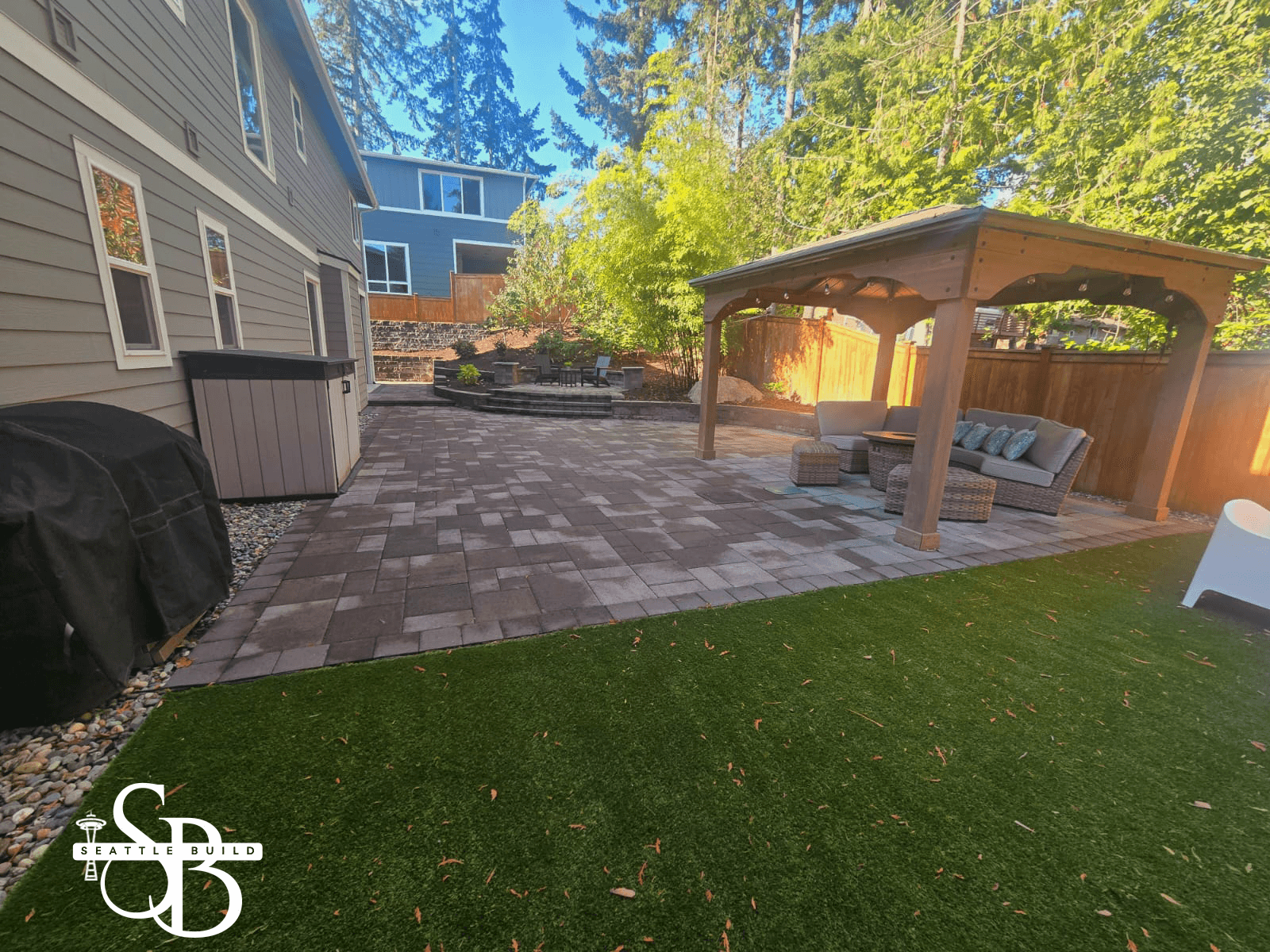 Modern two-story home with large glass windows, warmly lit interiors, and a balcony. Surrounded by trees and a manicured lawn at dusk. Cozy ambiance.