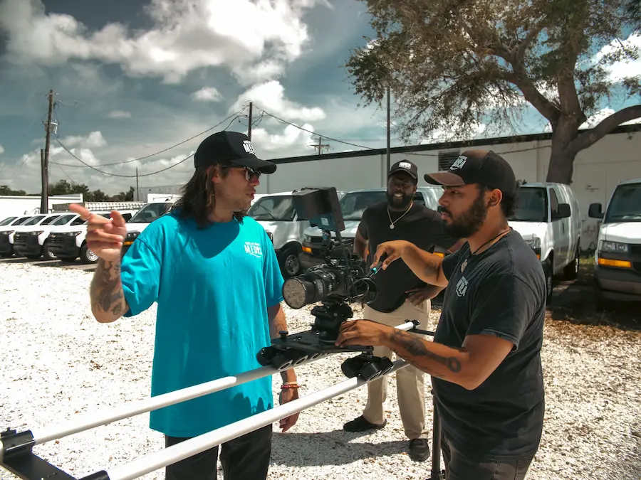 Two men are adjusting a camera on a dolly track in a gravel parking lot, showcasing a behind-the-scenes look at video production by Dream Wave Media in Bradenton, FL.