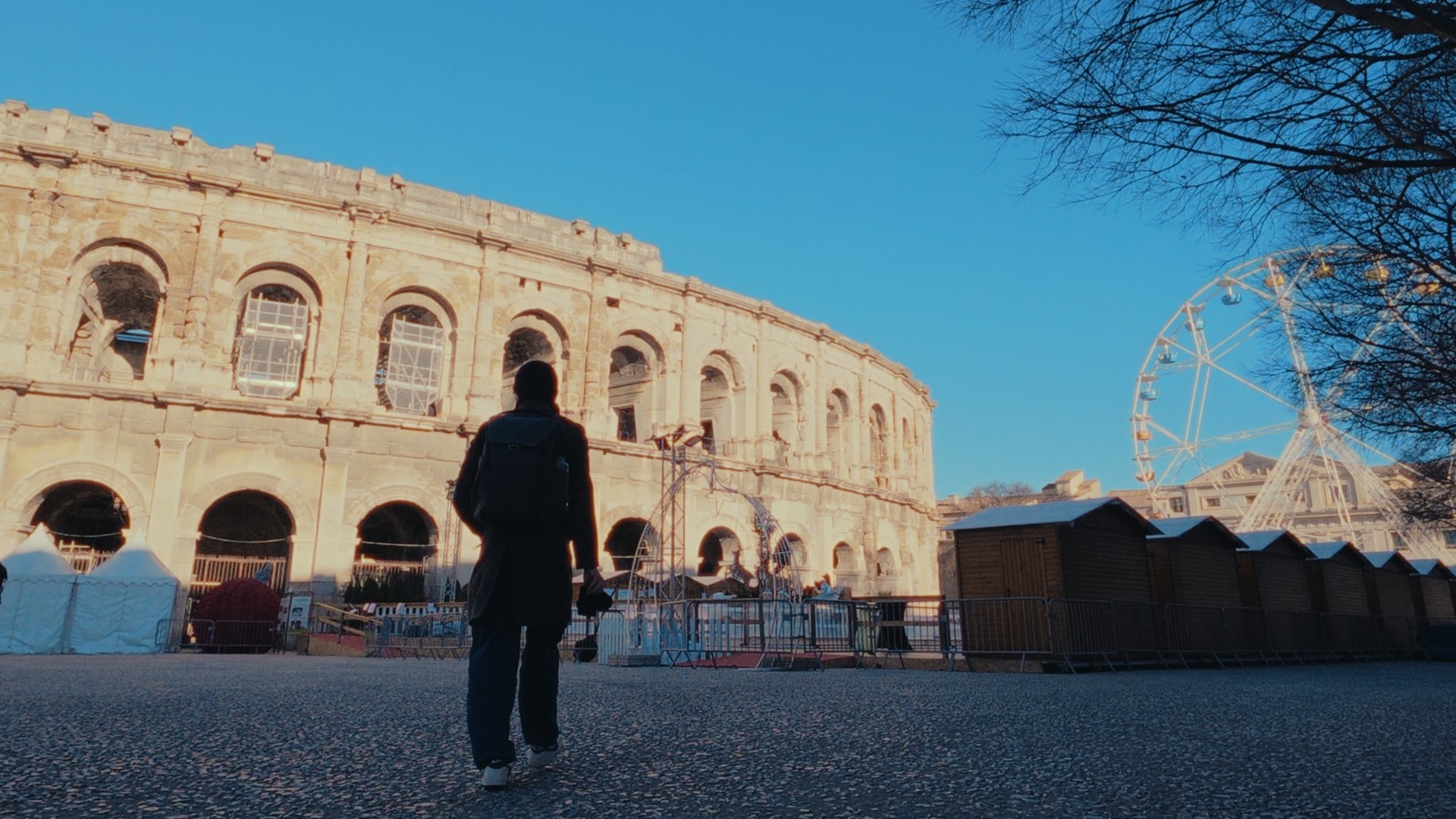 Silhouette d’un passant devant les arènes de Nîmes, près des installations d’un marché festif.