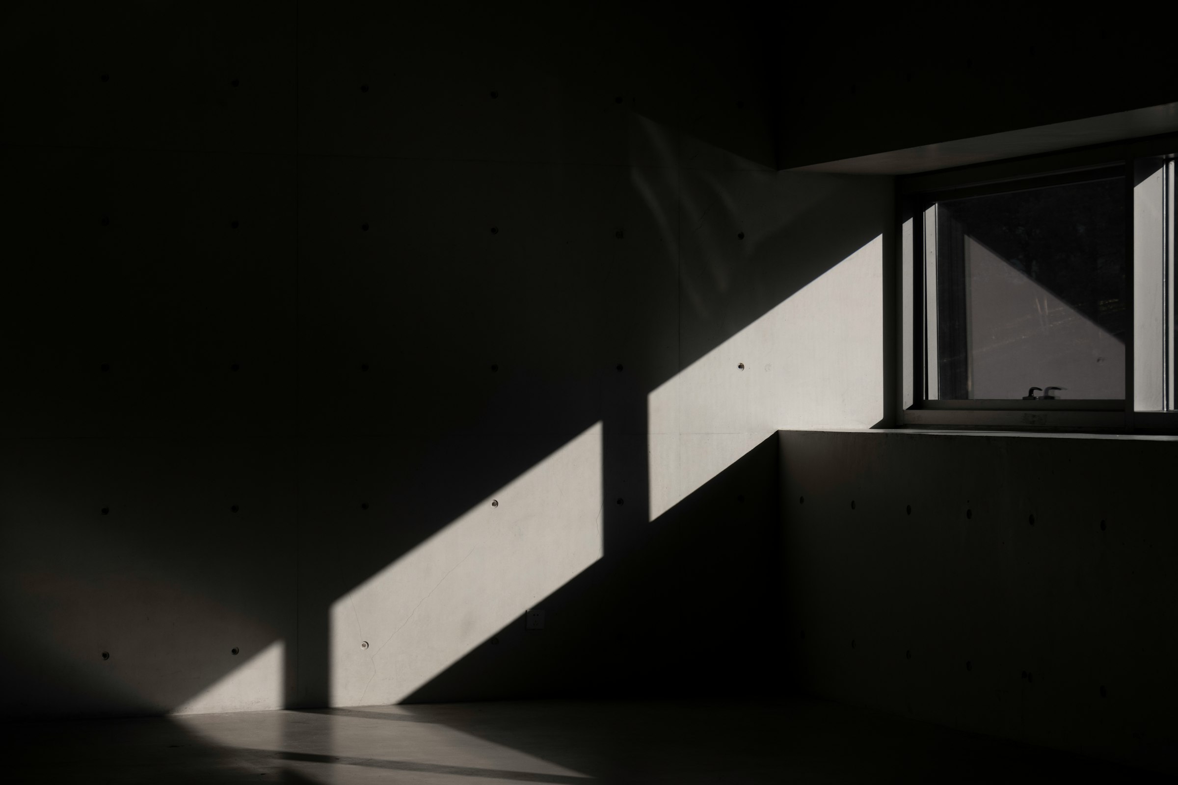 Low sun falling through a single window onto a dark concrete wall