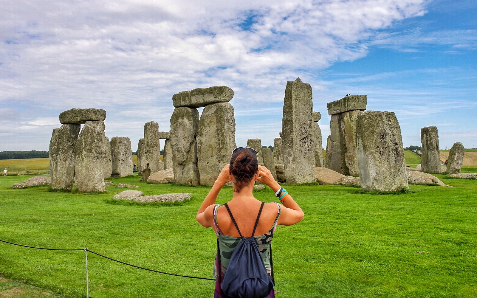 Visitor photographing Stonehenge with audio guide, Wiltshire, England.