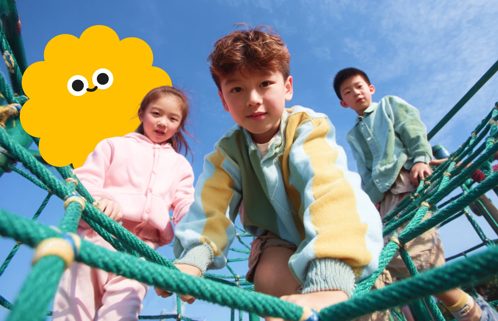 Three children play on a jungle gym under a sunny blue sky, smiling and enjoying their time together.