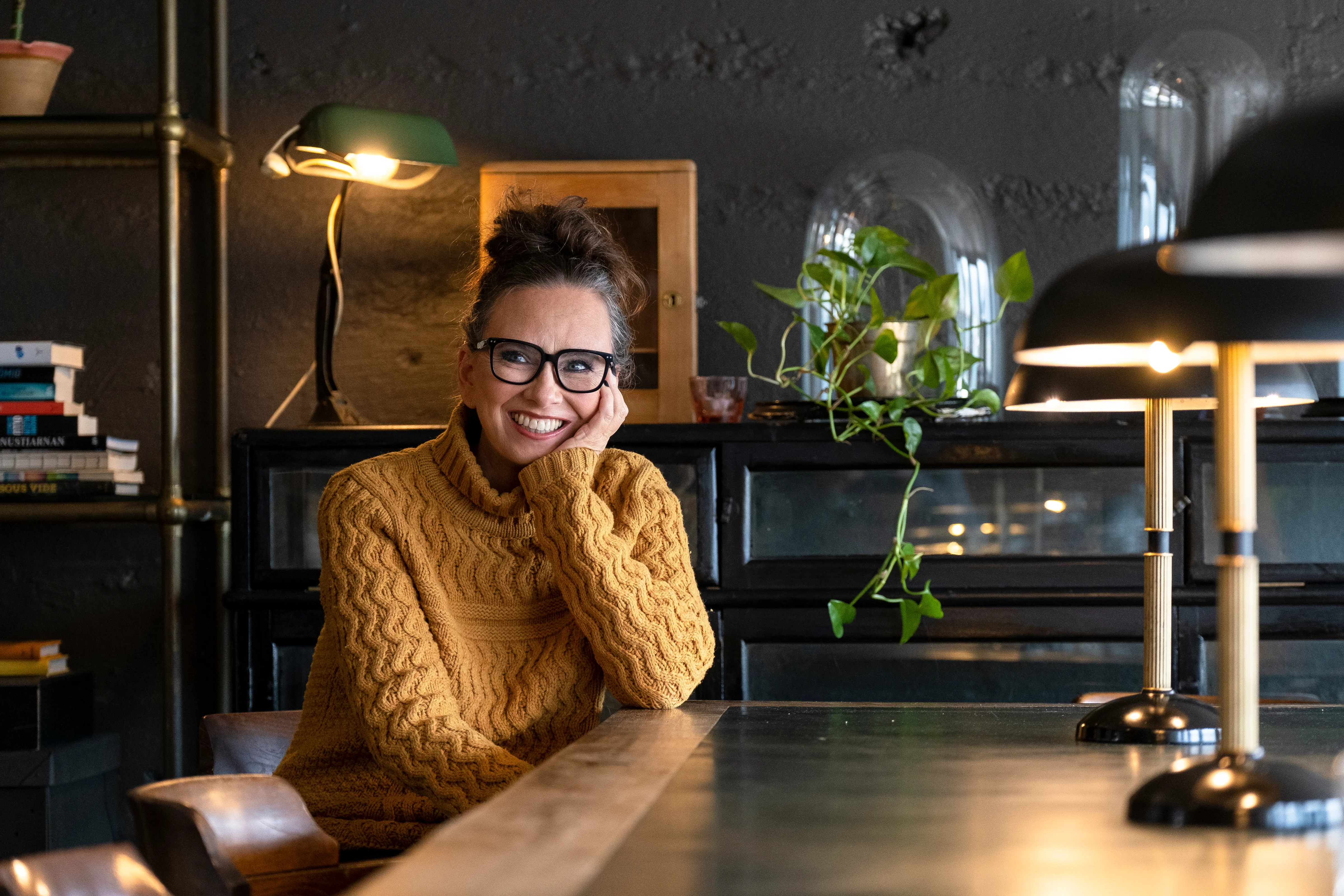 Author Yrsa Sigurðardóttir, co-founder of Iceland Noir, smiles at the camera wearing dark-framed glasses and a white polka-dot blouse against a plain grey background.