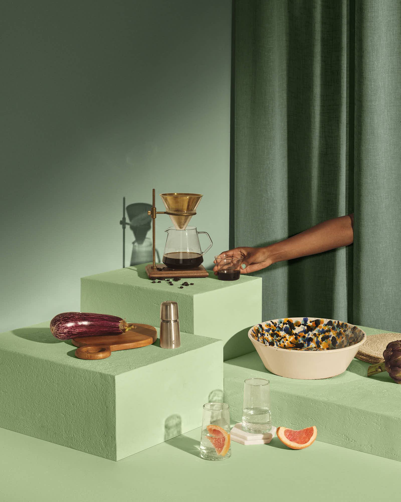 Modern kitchen still life with coffee brewing set, eggplant, and citrus on pastel blocks.