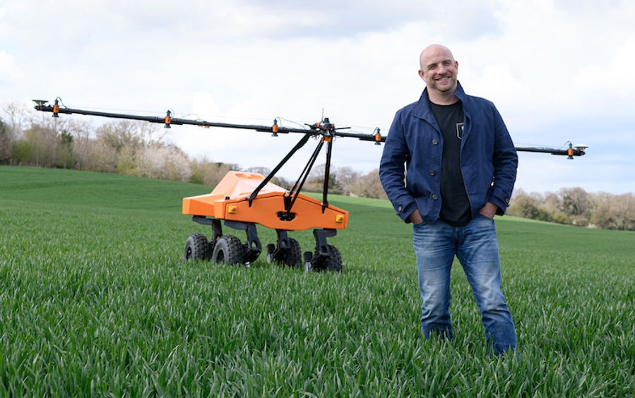 A man standing in front of an agricultural robot in a field of crops. 