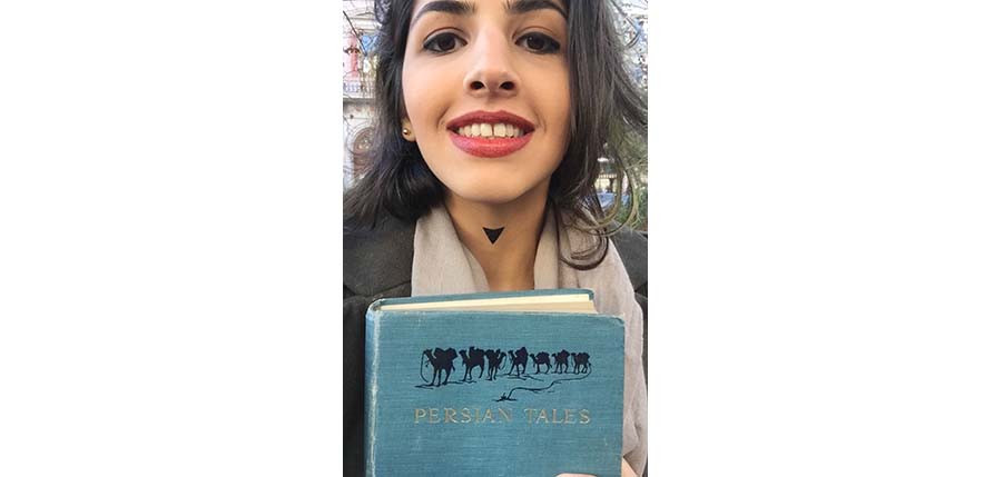 A photo of a smiling girl with a blue book in her hands on which there are some camels an the text: Persian Tales.