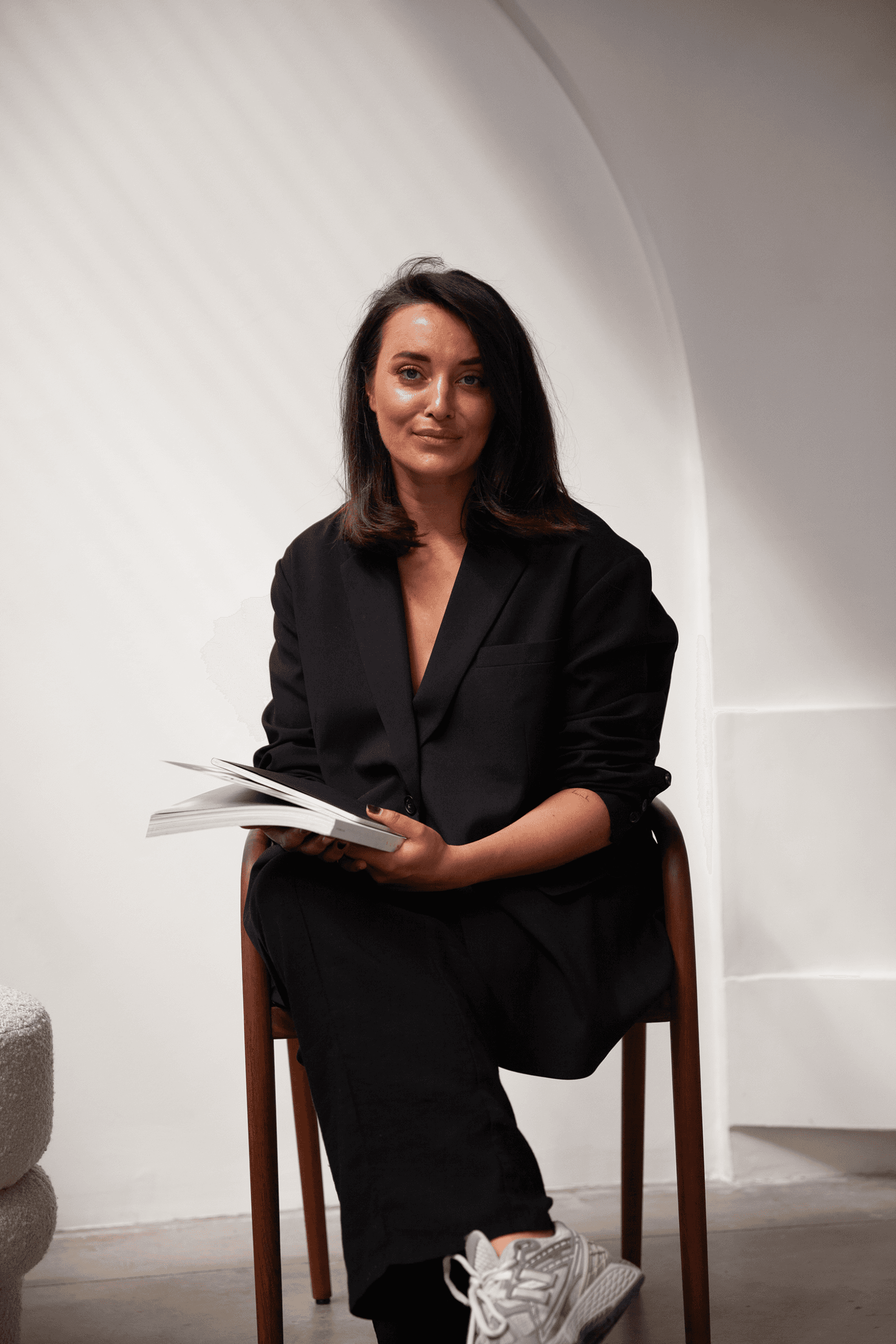 Woman in an oversized black blazer sitting on a chair holding an open notebook