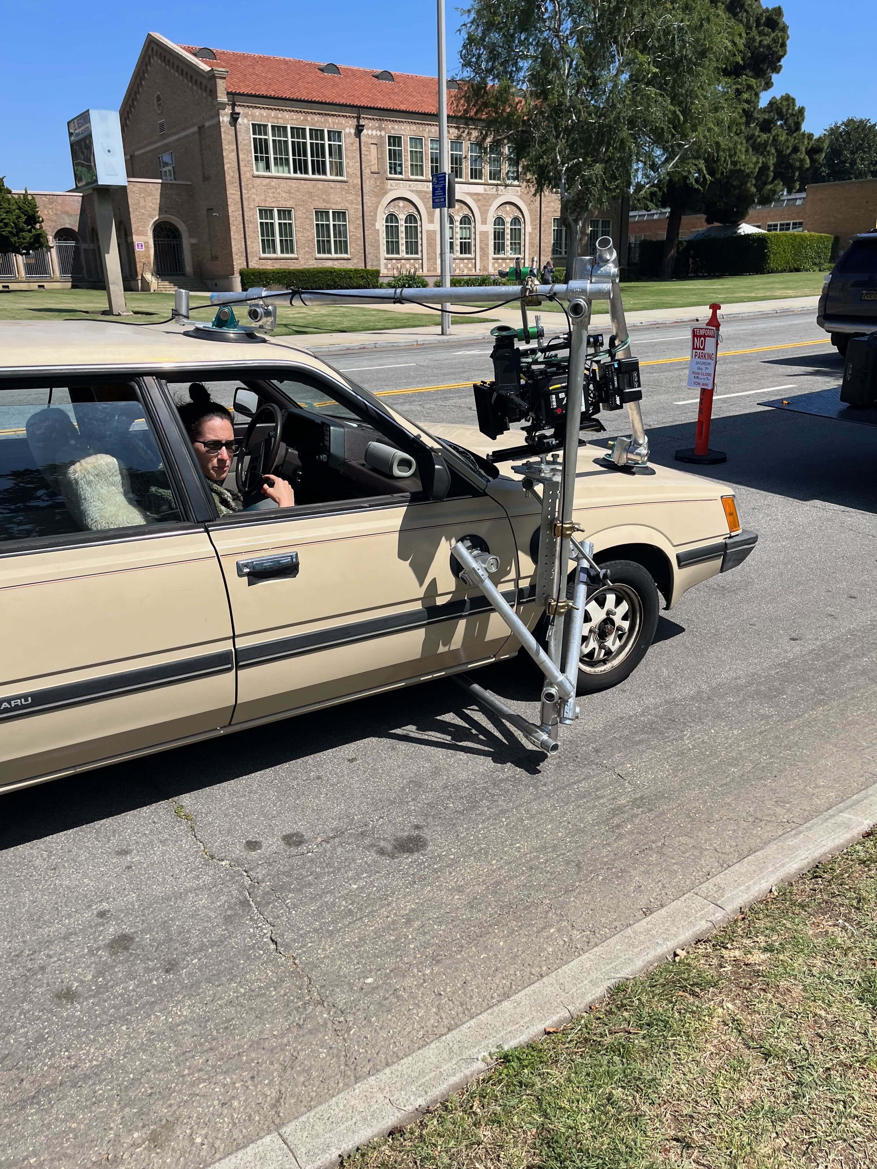 Side-mounted cinema camera on a beige sedan, supported by roof and hood suction cups and speed rails