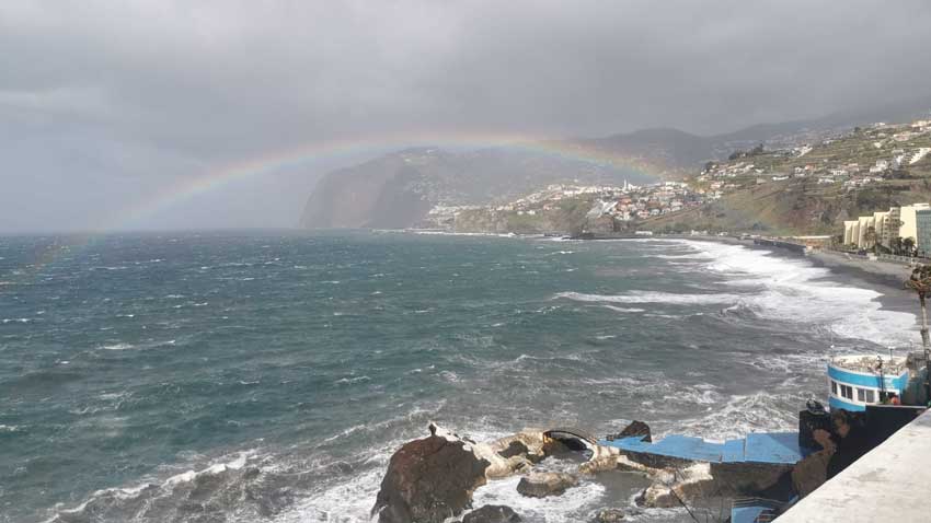 Rainbow over the ocean with a coastal town in the background. Calm day at the beach.
