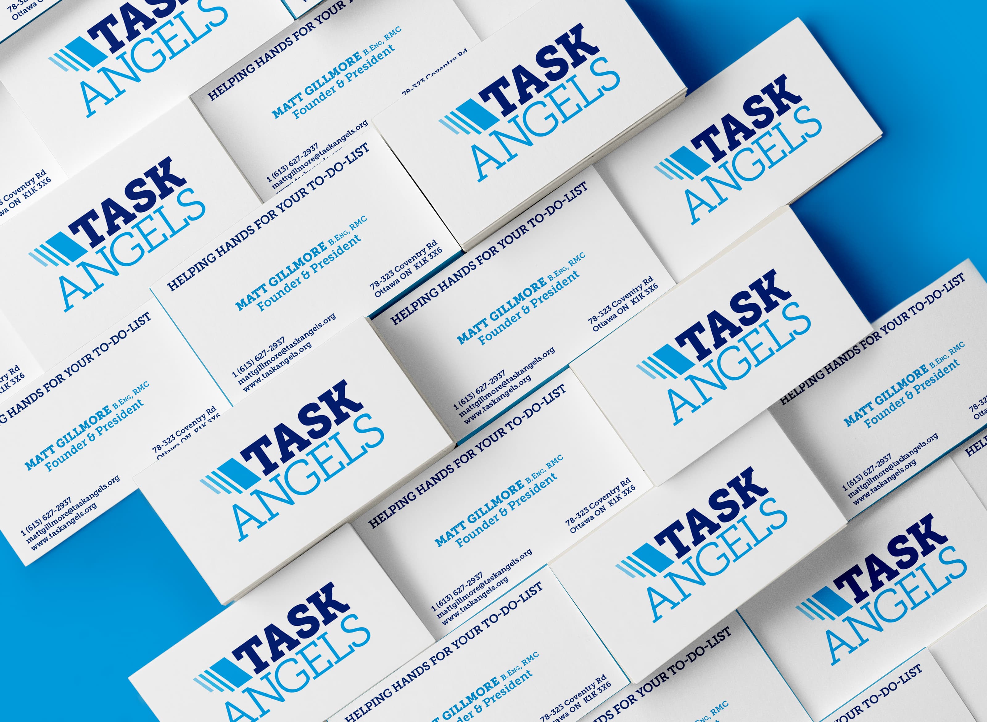 A scattered arrangement of business cards for 'Task Angels,' displayed on a bright blue surface. The cards feature a bold blue and light blue logo with the tagline 'HELPING HANDS FOR YOUR TO-DO LIST.' with contact information.