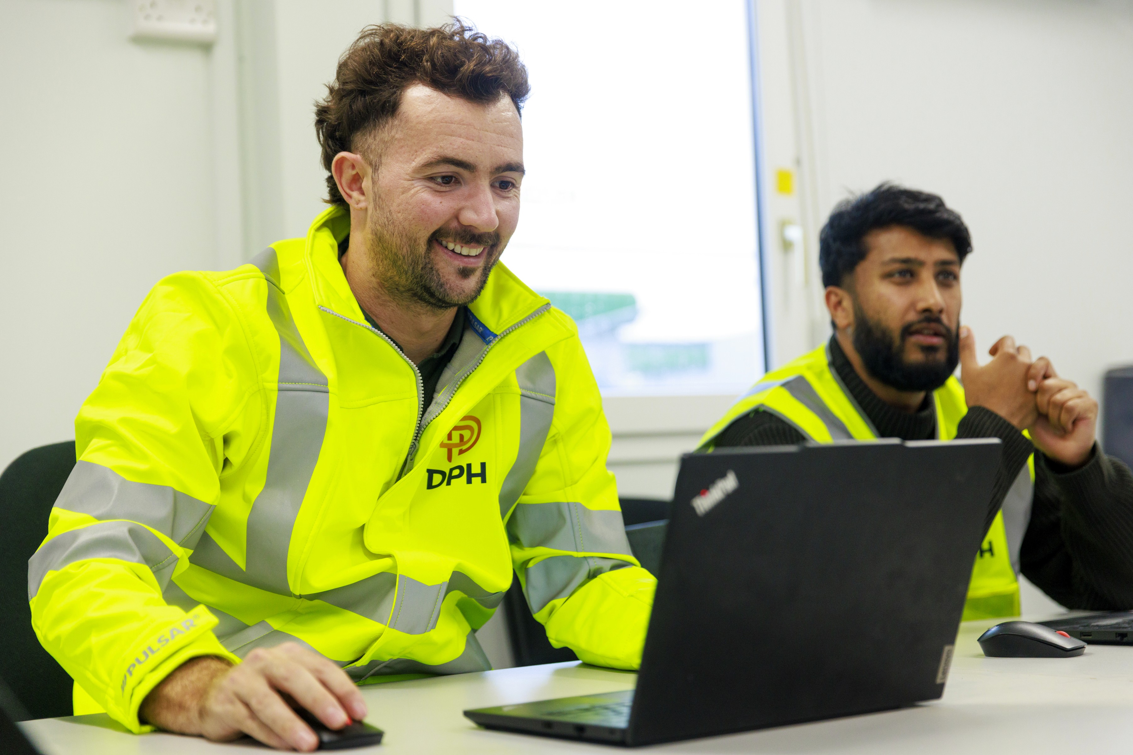 Modern glass building with illuminated facade and trees at sunset