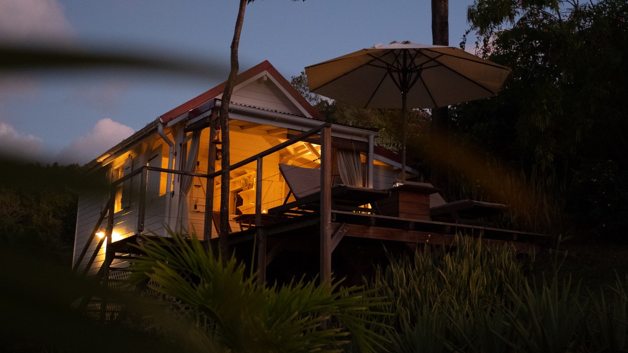 Lodge Rosewood illuminé en soirée dans un jardin tropical à Vieux-Habitants en Guadeloupe