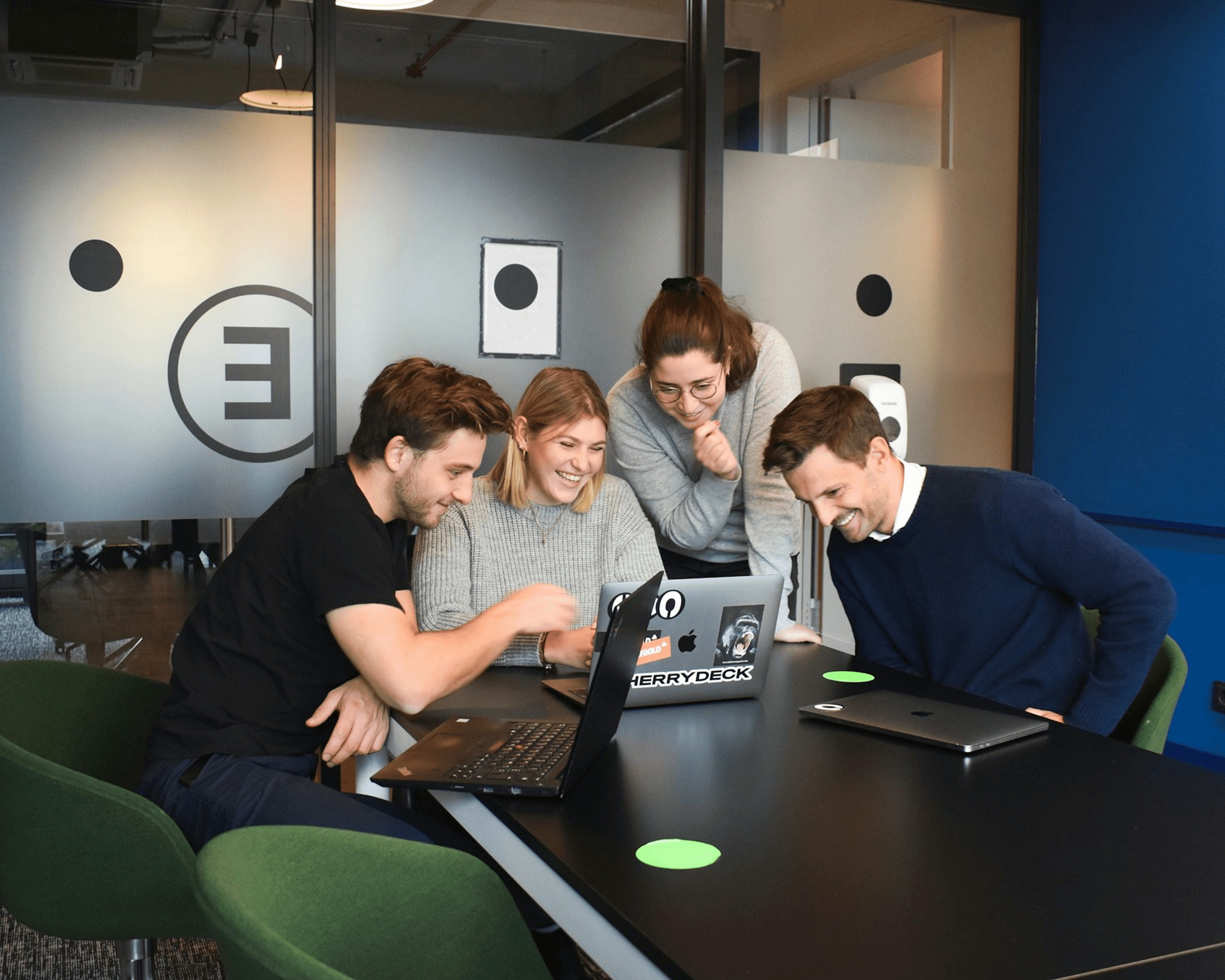 Four people collaborating around laptops in modern office