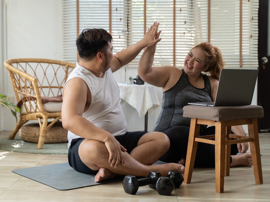 overweight couple high-fiving to celebrate as they complete their routine of simple exercises to lose weight at home