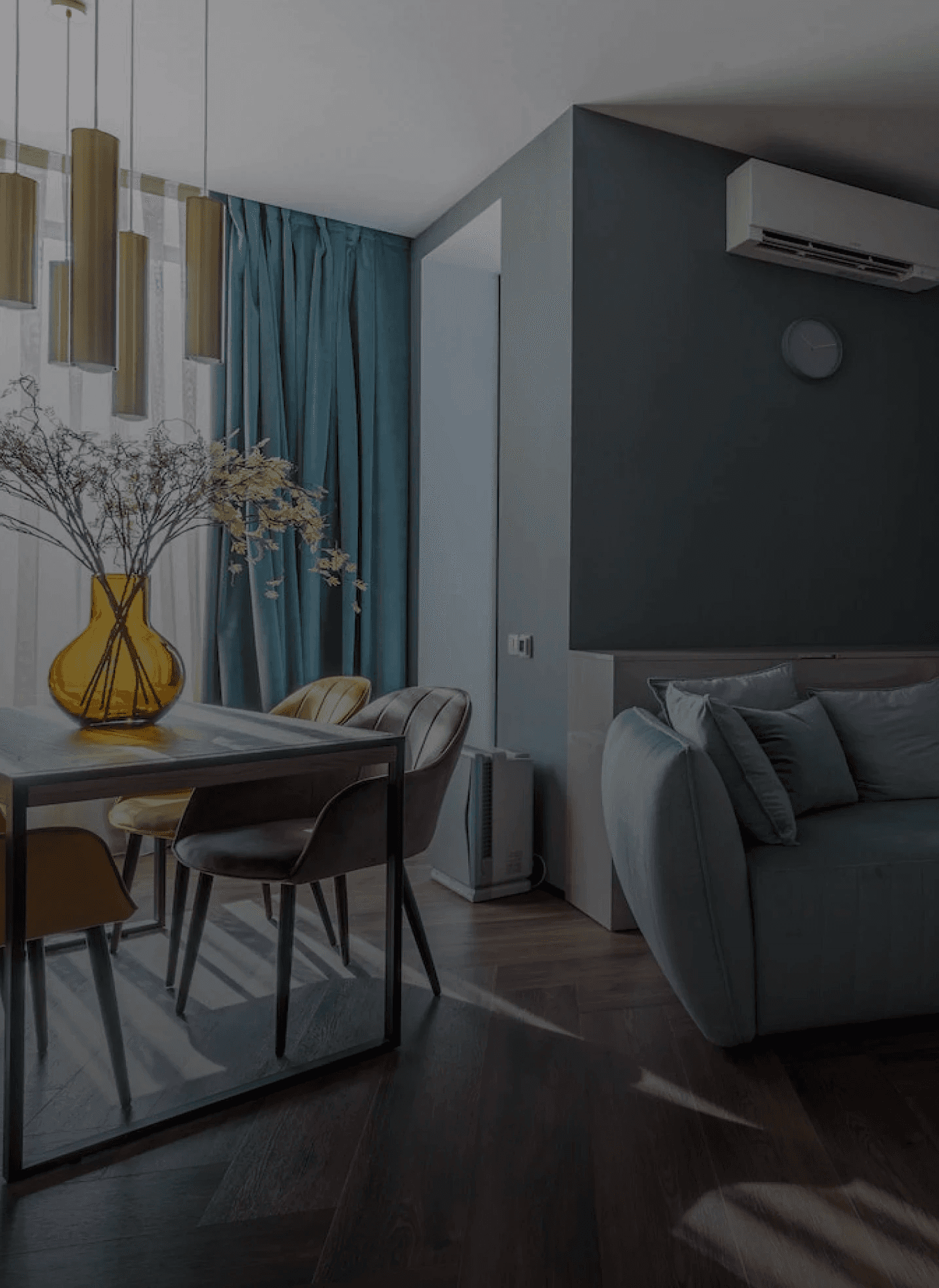 imagem da sala de uma casa elegante projetada por arquitetos. Imagem tem um sombreamento escuro para gerar contraste com o texto da seção. A sala apresenta cores pastéis em tons de azul, cinza e bege.